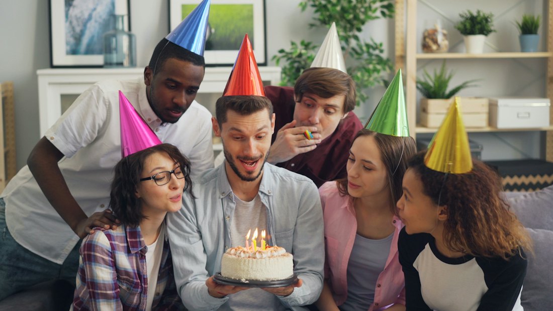 Friends in party hats around a birthday cake at home