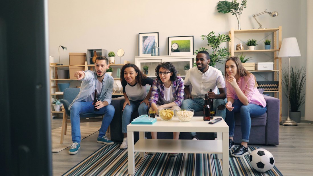 Friends on a sofa in a living room with snacks and drinks