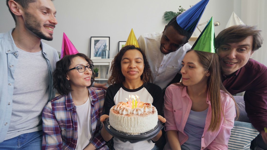 Friends gathered around a woman blowing out birthday candles