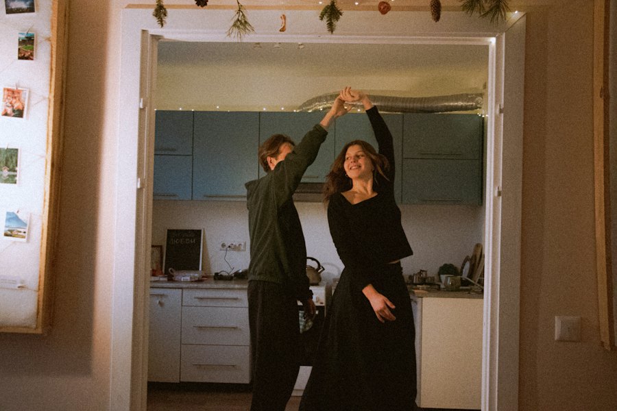 A couple dancing in a kitchen doorway at home, under fairy lights